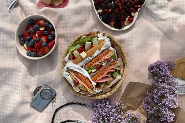Enjoy a delicious picnic spread with sandwiches, fruits, and lilacs, captured in a top view style.